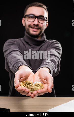 Portrait of man in glasses showing golden bitcoins in his hands isolated over black background Stock Photo