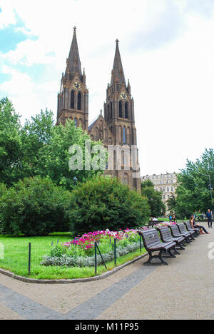 PRAGUE, CZECH REPUBLIC - JULY 21, 2009 Green park alley with benches with the view of Church of Saint Ludmila, people rest on benches Stock Photo
