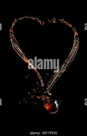Heart shaped coffee splash with a glass espresso cup on a black background. Liquid high-speed photography. Food in motion. Stock Photo