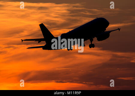 Silhouette of Airbus A320 passenger jet taking off in sunset with orange-lit clouds in background Stock Photo