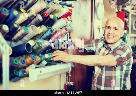 Mature diligent workman sewing leather boots on stitch lathe in workshop Stock Photo