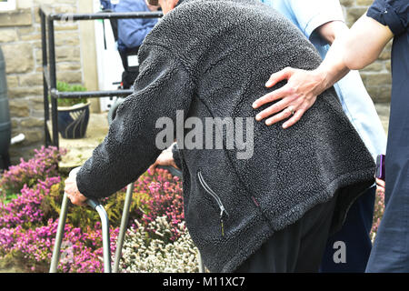 An elderly person is helped to walk with a carer and zimmer frame in a care home, UK Stock Photo
