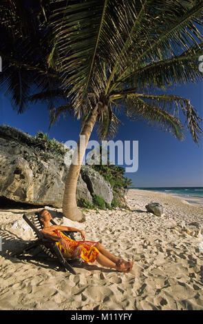Mexico. Yucatan Peninsula. Tulum. Woman in deck chair sunning at beach. Palm tree. Stock Photo