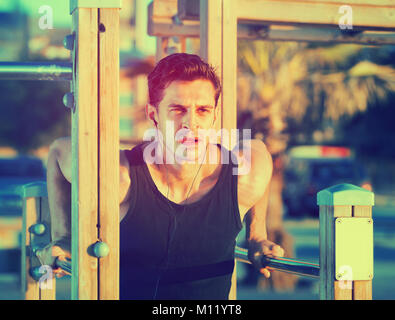 Happy cheerful positive  strong man doing parallel bar dips to music on sports ground on beach Stock Photo
