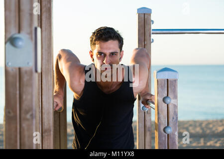 Physically fit man exercising with music outdoors doing triceps dips on parallel bars Stock Photo