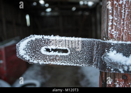 Old and weathered door hasp covered by frost with old abandoned garage in the background Stock Photo