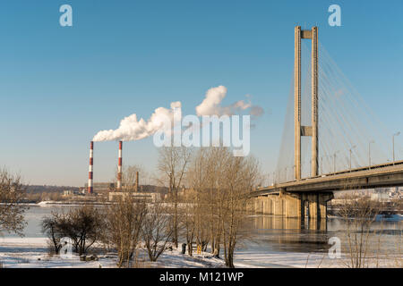 Two large smoking pipes on the river bank against the blue sky. White thick smoke. The Big Bridge over the River Stock Photo