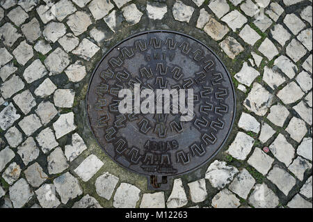 metal manhole cover in a cobbled street, close up. Stock Photo