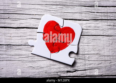 closeup of some pieces of a puzzle forming a heart on a white rustic wooden surface Stock Photo