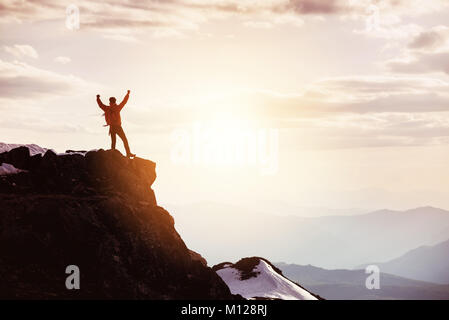 Man in winner pose at mountain top against mountains and sunset Stock Photo