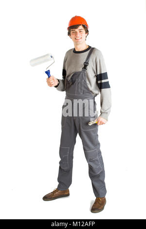 A young man in working grey clothes and orange hard helmet painting the walls in the room. Stock Photo