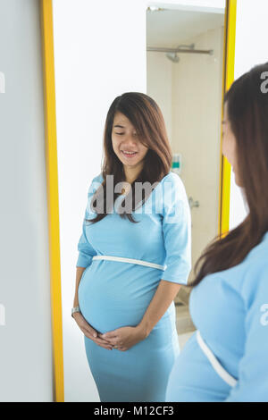 A portrait of asian pregnant woman posing infront of a mirror, smiling proudly Stock Photo