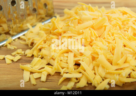 Close-up, detail, yellow grated cheese, hand grater on wooden board, food preparation Stock Photo