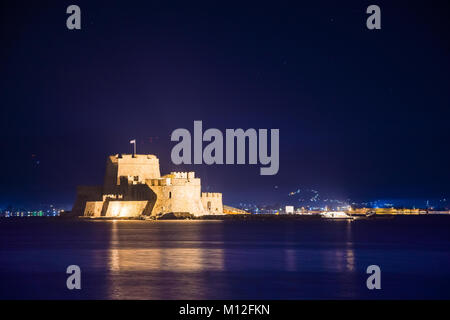 Illuminated old town of Nafplion in Greece with tiled roofs, small port, bourtzi castle, Palamidi fortress at night. Stock Photo