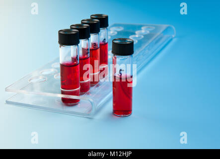 Red liquid samples in a transparent plastic tray on blue gradient background Stock Photo