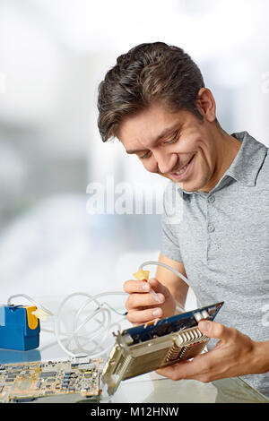 Smiling male tech cleans faulty computer processor in hardware repair workshop Stock Photo