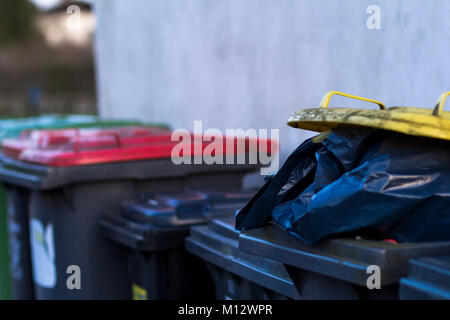 Row of overflowing rubbish bins with different colored lids and black bags of refuse. Stock Photo