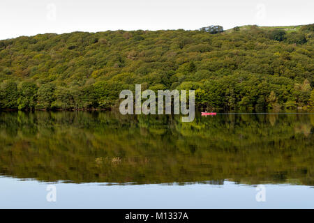 Coniston Water, UK - 15th September 2011: Two people pass in a red canoe on Coniston Water on a dead calm early autumn morning in the Lake District, Cumbria, UK. Boats can be hired from the lakeside, with various sizes of boat for hire, from small canoes and kayaks to large personal craft.