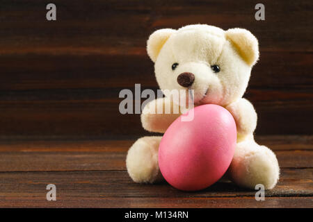 White teddy bear with a pink Easter egg on a brown wooden table Stock Photo