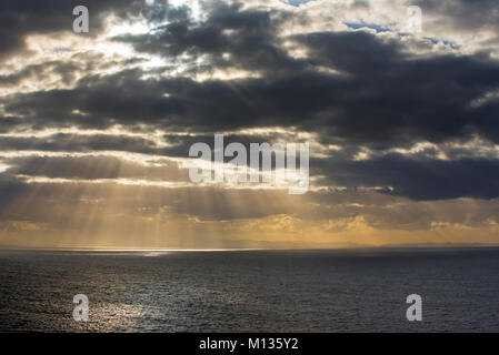 Sunrays bursting through dense sheet of rain clouds over sea water at sunset Stock Photo