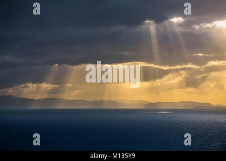 Sunrays bursting through dense sheet of rain clouds over sea water at sunset Stock Photo