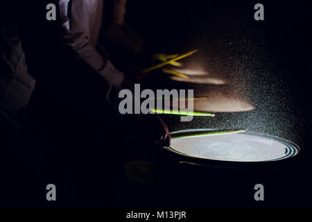 The drum sticks are hitting on the snare drum with splash water in low light background