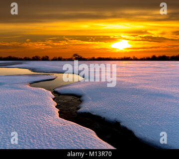 Sunset over brook across winter meadow Stock Photo
