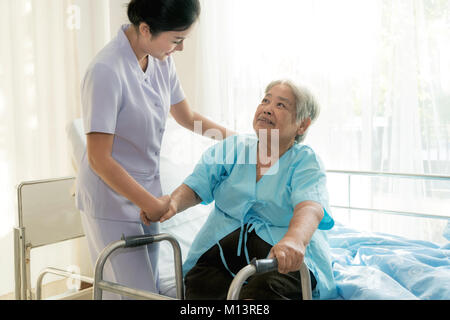 Asian young nurse supporting elderly patient disabled woman in using walker in hospital. Elderly patient care concept. Stock Photo