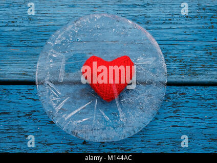 the warm red heart lies surrounded by the sharp cold of ice on a blue table Stock Photo
