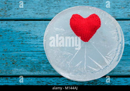the warm red heart lies surrounded by the sharp cold of ice on a blue table Stock Photo