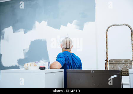 Rear view of a male decorator looking at the painting he hasd done on a wall. Stock Photo
