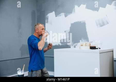 Male decorater is having a break from painting. He is drinking tea and eating a fruit scone. Stock Photo