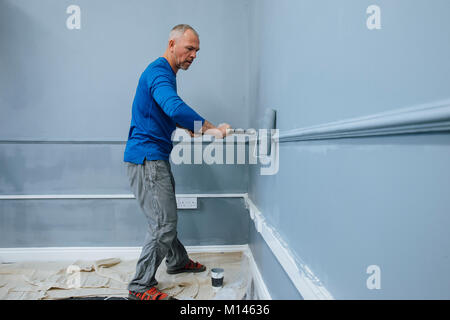 Male builder is using a roller to paint walls of an interior. Stock Photo