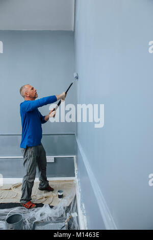 Male builder is using a roller to paint walls of an interior. Stock Photo