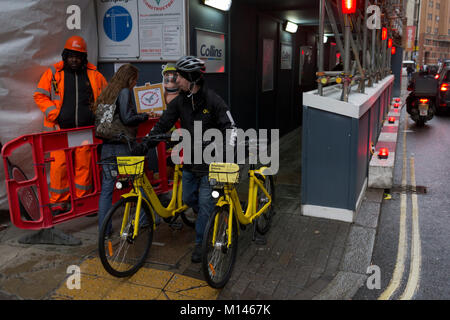 An Ofo employee pushes two rental bikes along a street, 24th January 2018, in London, England. ofo is a Beijing-based bicycle sharing company founded in 2014. It operates over 10 million yellow-colored bicycles in 250 cities and 20 countries, as of 2017. The dockless ofo system uses a smartphone app to unlock bicycles, charging an hourly rate for use. As of 2017, the company is valued at $3 billion and has over 62.7 million monthly active users Stock Photo