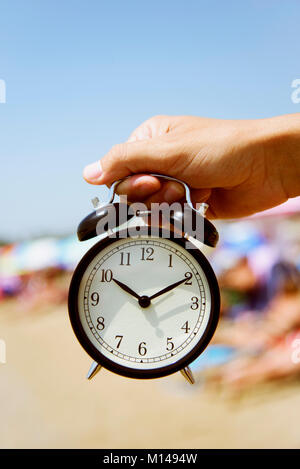 closeup of a young caucasian man with an alarm clock in his hand on the beach, next to the seashore Stock Photo