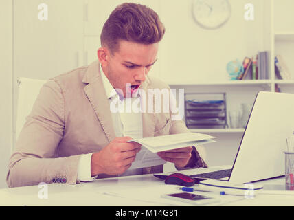 Upset sad young man having business problems with documents at workplace Stock Photo
