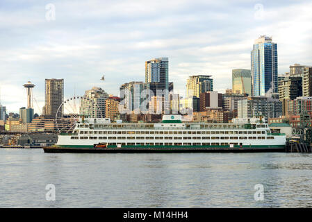 The Port of Seattle and waterfront with a ferry boat landing surrounded by the Space Needle and Big Wheel, and the city downtown skyscrapers Stock Photo