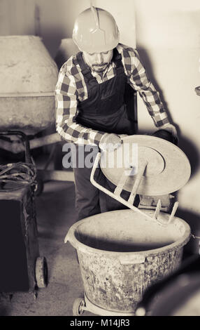 Young smiling male using concrete mixer for construction work at workshop Stock Photo