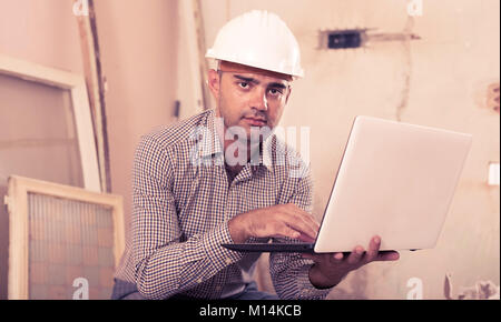 Portrait of master working at the notebook in shirt and helmet Stock Photo