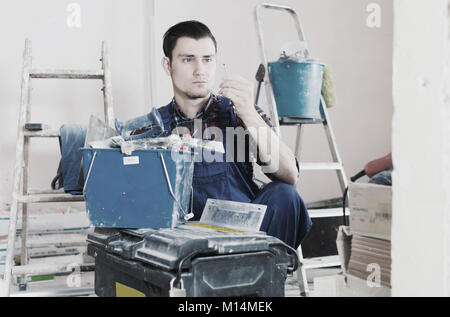 Positive adult worker repairing room and looking for necessary tool in toolbox Stock Photo