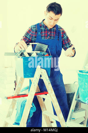 Young attentive builder handyman choosing necessary tool in toolbox Stock Photo