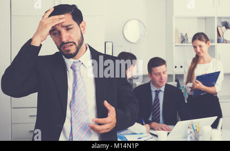 Business team tensely solving problems in office with upset man foreground Stock Photo
