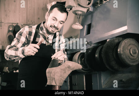 positive spanish male worker fixing failed shoes in shoe repair workshop Stock Photo