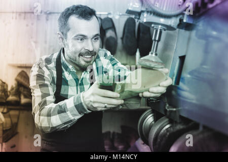Smiling american male worker fixing failed shoes in shoe repair workshop Stock Photo