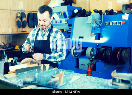Smiling male worker fixing failed shoes in shoe repair workshop Stock Photo