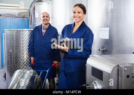 Glad diligent positive female winery worker taking notes while male one working in fermentation section Stock Photo