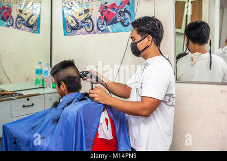 A Filipino barber cuts a high and tight fade hairstyle on a teenage boy in Barretto, Luzon, Philippines. Stock Photo