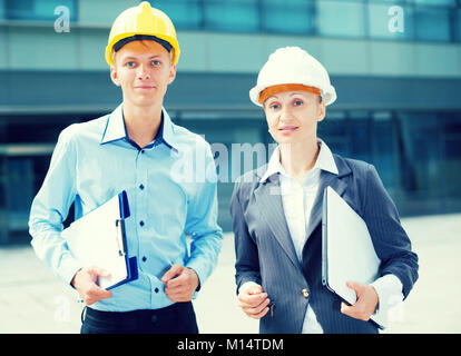 Portrait of smiling architectors who standing with folder and laptop near the building. Stock Photo