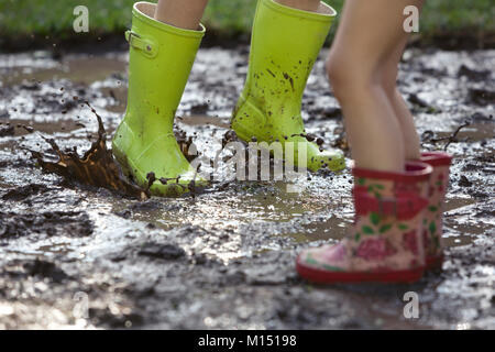 Children jumping in a muddy puddle, wearing wellington boots Stock Photo
